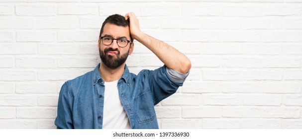 Handsome man with beard over white brick wall with an expression of frustration and not understanding