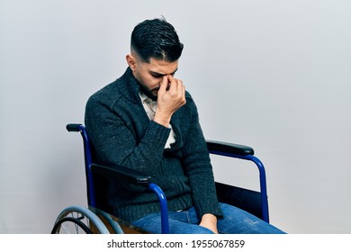 Handsome man with beard sitting on wheelchair tired rubbing nose and eyes feeling fatigue and headache. stress and frustration concept. 