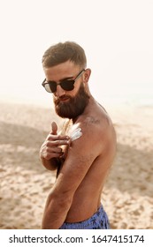 Handsome Man With Beard, In Sunglasses Sunbathing With Sunscreen Lotion Body In Summer. Male Fitness Model Tanning Using Solar Block Cream For Healthy Tan. Skincare. Sun Skin Protection 