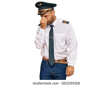 Handsome Man With Beard Wearing Airplane Pilot Uniform Tired Rubbing Nose And Eyes Feeling Fatigue And Headache. Stress And Frustration Concept. 