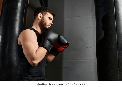 A handsome man with a beard wearing a black tank top punches a boxing bag in a gym while sporting vibrant red gloves. - Powered by Shutterstock
