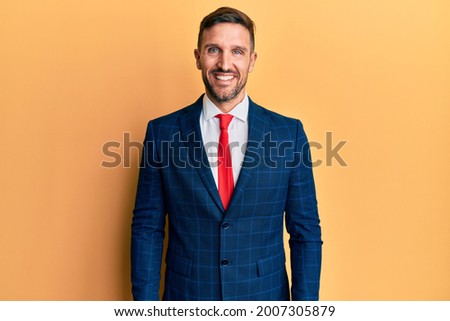 Handsome man with beard wearing business suit and tie looking positive and happy standing and smiling with a confident smile showing teeth 
