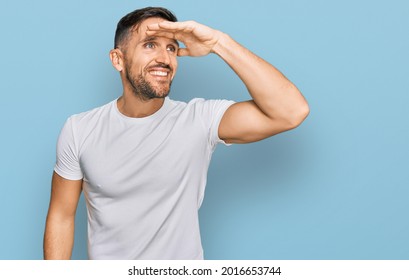 Handsome man with beard wearing casual white t shirt very happy and smiling looking far away with hand over head. searching concept.  - Shutterstock ID 2016653744
