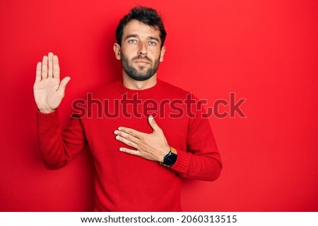 Handsome man with beard wearing casual red sweater swearing with hand on chest and open palm, making a loyalty promise oath 