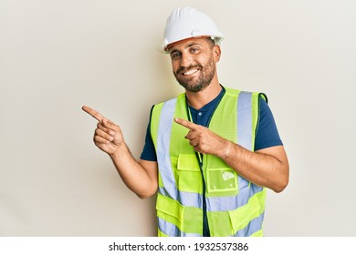 Handsome man with beard wearing safety helmet and reflective jacket smiling and looking at the camera pointing with two hands and fingers to the side.  - Powered by Shutterstock