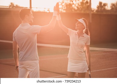 Handsome man and beautiful woman are giving high five and smiling while playing tennis on tennis court outdoors - Powered by Shutterstock