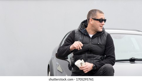 Handsome Man In Black Drinking Coffee, Smoking Cigarette And Sitting On The Car