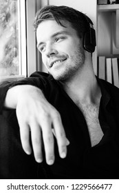 Handsome Man With Black Shirt Sitting In Bay Window Seat Listening To Music On Headphones