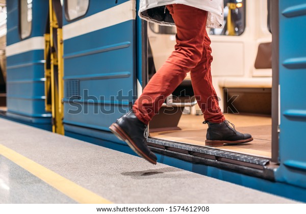 Handsome man in black shoes, burgundy pants and white\
jacket runs into a subway train. Male is late for work. Selective\
focus on the left leg. Public transport and mobility in urban\
concept. Close up.