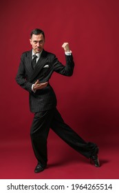 Handsome man in black stripped suit smiling on red background. Attractive professional tango dancer  posing in a dancing movement while looking at camera.