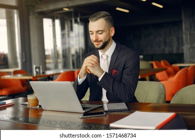 Handsome man in a black suit. Businessman working in a cafe - Shutterstock ID 1571468734