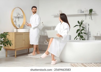 Handsome man brushing teeth while his wife using laptop in bathroom