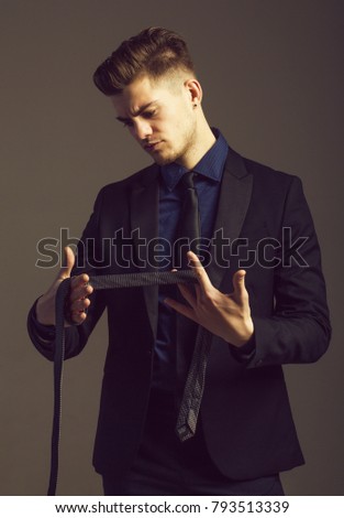 Handsome man or businessman, young, caucasian, adult, male fashion model with blond hair in suit and necktie keeps tie in hands on grey background