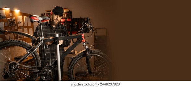 Handsome man in cap, handyman standing with a bicycle in the garage at home. Bicycle repairing and diy concept. Banner. Copy space - Powered by Shutterstock