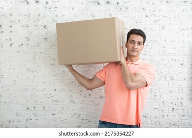 Handsome Man Carrying Heavy Box In Front Of White Brick Wall Background