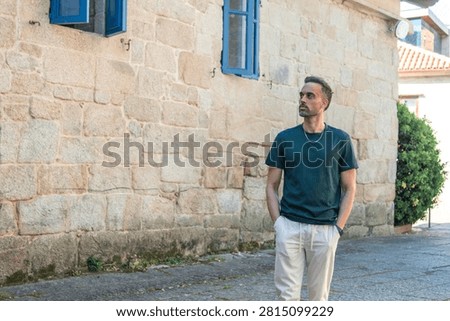 Handsome man casually walking through the city looking to the side, glancing at the houses