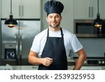 Handsome man chef in uniform cooking in the kitchen. Restaurant menu concept. Hispanic man in baker uniform. Cooking and culinary. Male chef in working uniform, black apron, chef hat.