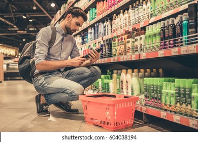 Handsome Man Is Choosing Cosmetics While Doing Shopping At The Supermarket