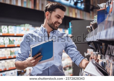 Handsome man is choosing a magazine and smiling while doing shopping at the supermarket