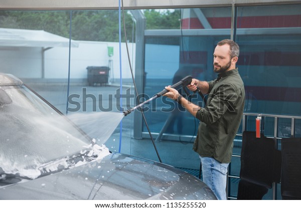 handsome man cleaning car front window at car wash\
with high pressure water\
jet