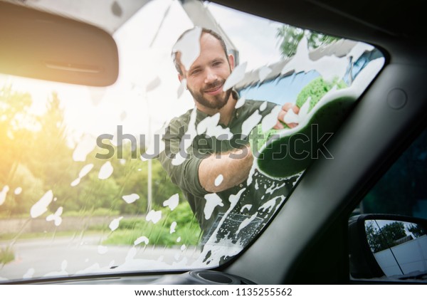 handsome man cleaning car front window with rag and\
soap at car wash