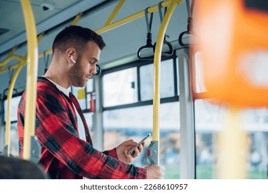 Handsome man commuting to work by bus while using a smartphone. Bearded hipster guy is reading emails or typing a message on a mobile phone during his ride. People travel transport concept. - Powered by Shutterstock