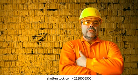 Handsome Man In A Construction Helmet And A Goggle, Middle Aged Builder, Choosing A Profession Isolated On Yellow Brick Wall Background.