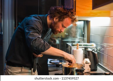 Handsome Man Cooking At The Kitchen, Man Curly Hair Style, Man In Black Shirt, Bearded Man, Home Party, Prepare Dinner, Pan, Pasta, Kettle, Delicious, Food, Evening, Pretty, Seriously, Concentration