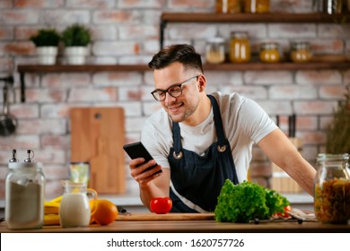 Handsome Man Cooking In The Kitchen And Talking On His Mobile Phone.