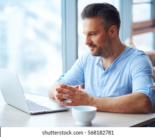 Handsome man with cup of coffee using laptop at home.