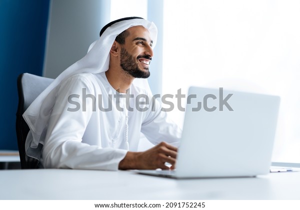 Handsome man\
with dish dasha working in his business office of Dubai. Portraits\
of a successful businessman in traditional emirates white dress.\
Concept about middle eastern\
cultures