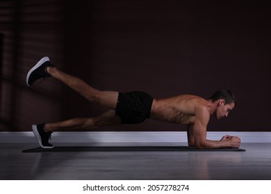 Handsome Man Doing Plank Exercise With Leg Lift On Floor Indoors