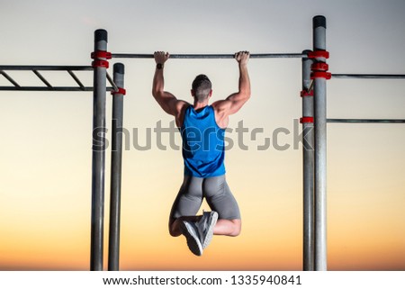 Handsome man doing pull-ups at outside training park - concepts of calisthenics and sport