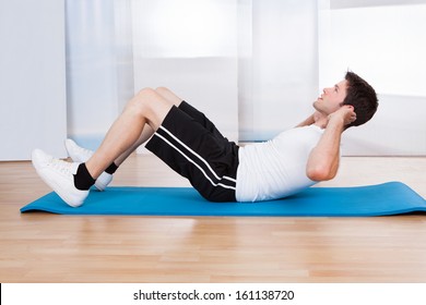 Handsome Man Doing Sit-ups On A Blue Exercise Mat