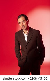 Handsome man dressed elegant classic suit standing on red background in spot of light with inquiring look at camera