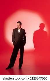 Handsome man dressed elegant classic suit standing in spot of light on red background with inquiring look at camera