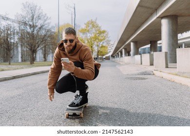 Handsome man dressed in style rides an skateboard and looks into his smartphone - Powered by Shutterstock