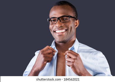 Handsome man dressing up. Handsome young black man dressing up his shirt and smiling at camera while standing against grey background - Powered by Shutterstock