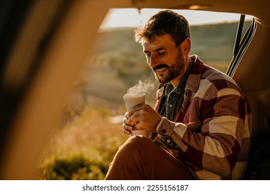 Handsome man drinking coffee while sitting in a car and enjoying the sunset. - Powered by Shutterstock