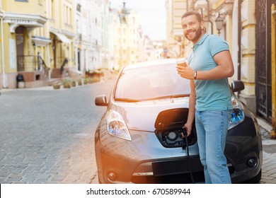 Handsome man drinking coffee while charging electric car