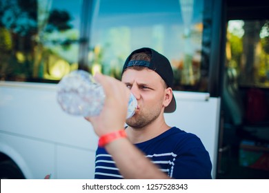 Handsome Man Drinking Water After Running Outdoors On The Background Of The Bus, Tourist.