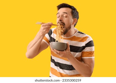 Handsome man eating Chinese noodles on yellow background - Powered by Shutterstock