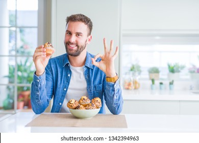 Handsome Man Eating Chocolate Chips Muffin Doing Ok Sign With Fingers, Excellent Symbol