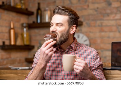 Handsome Man Eating Chocolate Muffin Sitting With Coffee At The Kitchen