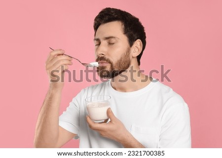 Handsome man eating delicious yogurt on pink background