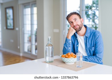 Handsome Man Eating Pasta With Meatballs And Tomato Sauce At Home With Hand On Chin Thinking About Question, Pensive Expression. Smiling With Thoughtful Face. Doubt Concept.