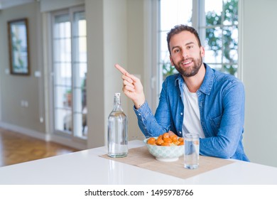 Handsome Man Eating Pasta With Meatballs And Tomato Sauce At Home With A Big Smile On Face, Pointing With Hand And Finger To The Side Looking At The Camera.