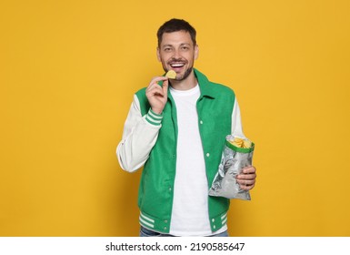Handsome man eating potato chips on orange background