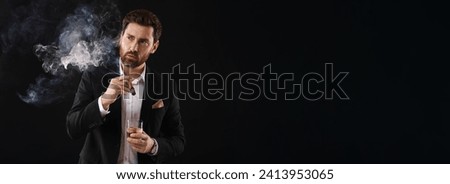 Handsome man in elegant suit with glass of whiskey smoking cigar on black background