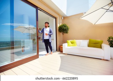 handsome man enjoys life on rooftop terrace, with open space kitchen and sliding doors